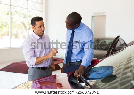 middle aged man talking to african car salesman inside showroom