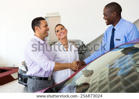 african car salesman handshaking with happy couple