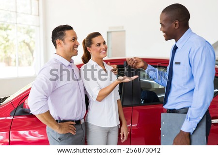 car salesman handing over new car key to couple in car showroom