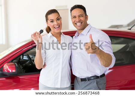 cheerful middle aged couple showing their new car key at dealership