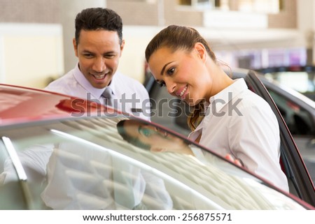 friendly middle aged vehicle dealer showing young woman new car
