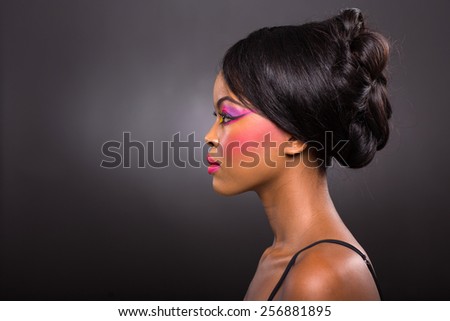side view of young african woman with colorful make-up on black background