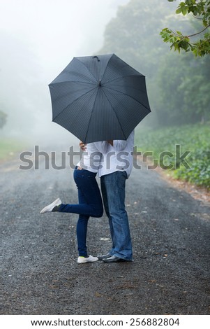 romantic young couple hiding behind the umbrella in the rain