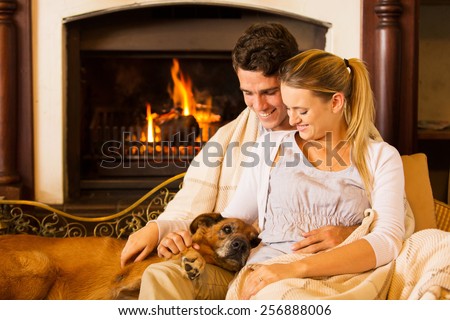 beautiful young couple sitting by fireplace with their pet dog at home