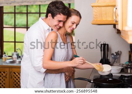 romantic young man hugging girlfriend while she cooks for breakfast