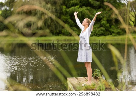 beautiful young woman with arms outstretched by the lake outdoors