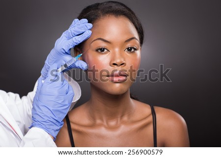 cosmetic surgeon injecting african american girl face on black background