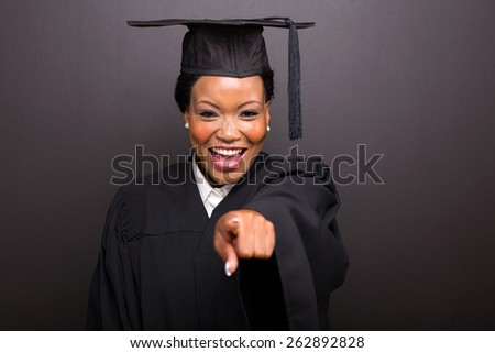 smiling female college graduate pointing isolated on black background
