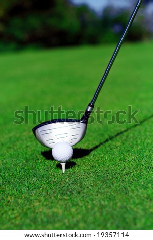 close up of a golf club, ball and tee on green grass. the golf club about to strike the ball