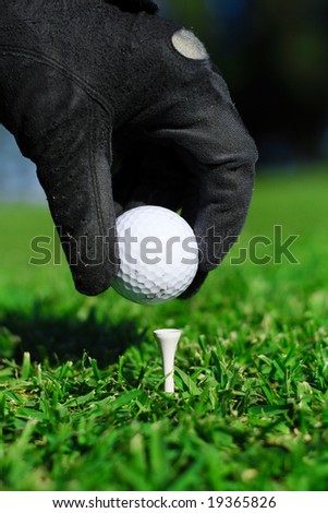 a hand with glove picking up a white golf ball to put on a tee
