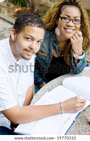Two african college students friends study a book together outdoors