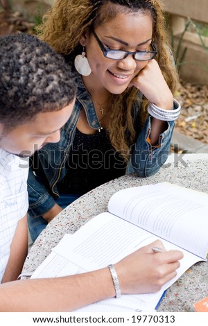 Two african college students friends study a book together outdoors