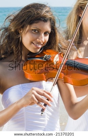 two beautiful young woman play violin on beach