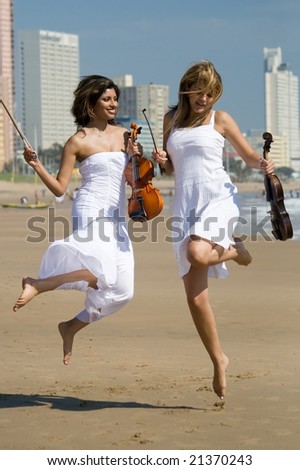 two beautiful young woman jump on beach with violin