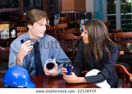 A handsome business construction manager and indian female construction worker in a cafe looking at blueprint