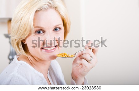 young blond beautiful woman sitting by breakfast table and eating cereal