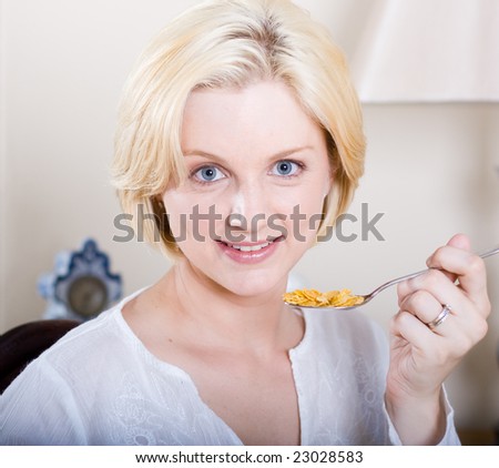 young blond beautiful woman sitting by breakfast table and eating cereal