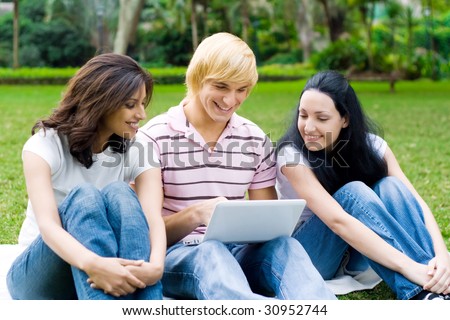 group of young college students use laptop on grass