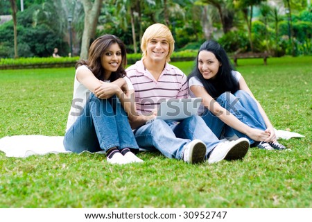 group of young college students use laptop on grass