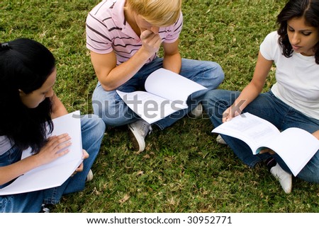 group of college students sitting in circle and reading book in the park