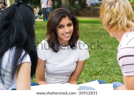 group of college students sitting on grass and reading book in the park