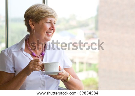 happy smiling woman drinking coffee by the window