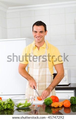 happy young man chopping vegetables in kitchen