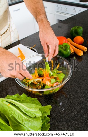 young man making green salad in kitchen