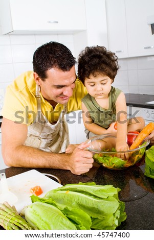 father and son making green salad together in modern kitchen