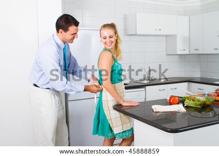 caring husband helping wife tie up apron in kitchen