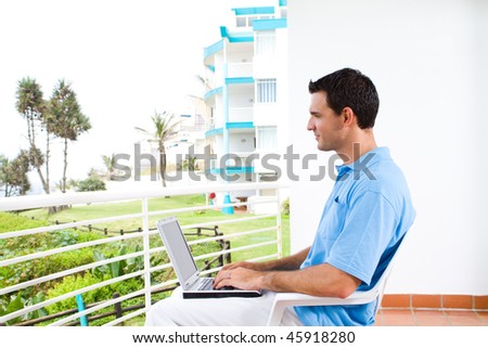 smart young man using laptop on balcony with sea view behind
