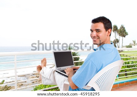 casual young man using laptop on balcony with sea view behind
