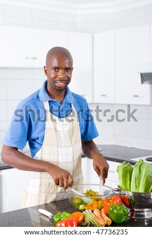 happy young african american man making a healthy salad in kitchen