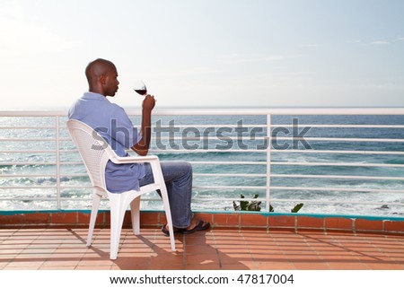 african american man drinking wine and viewing seascape