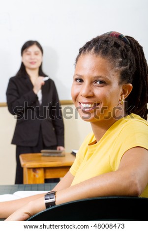 adult student in classroom, background is teacher standing by white board