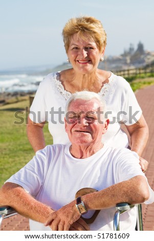 Disabled senior man being pushed by his loving wife at beach on sunny day
