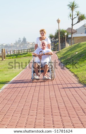 senior woman pushing her disabled husband on wheelchair