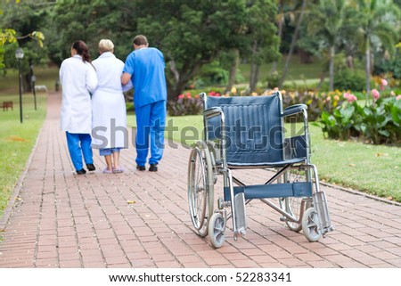 caring doctor and nurse helping senior patient get up from wheelchair and walk