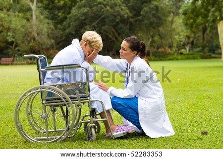 caring young female doctor comforting a lonely disabled senior patient outdoors