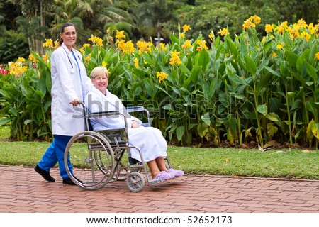 friendly and caring female doctor push senior patient on wheelchair outdoors for a walk