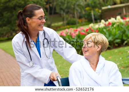 friendly female doctor pushing happy senior patient in wheelchair outdoors