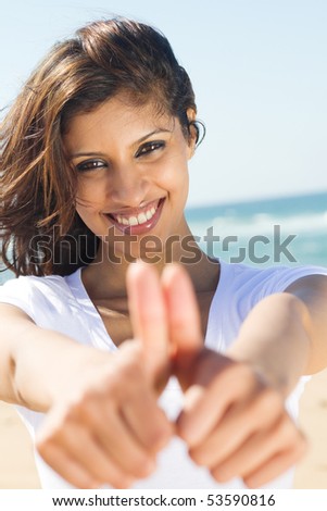 happy young woman giving thumbs up hand sign on beach