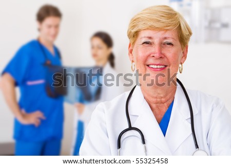 happy senior medical doctor, background is her young colleagues looking at x ray