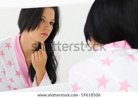 young woman checking her skin acne in mirror