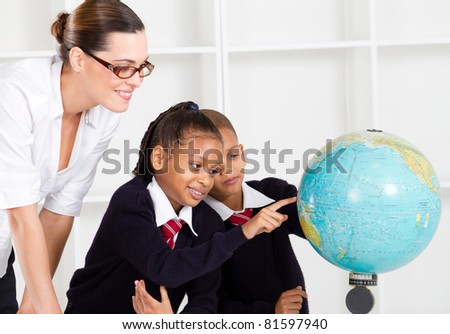 elementary geography teacher and students looking at globe in classroom