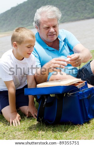 grandfather teaching grandson how to prepare fishing tackles