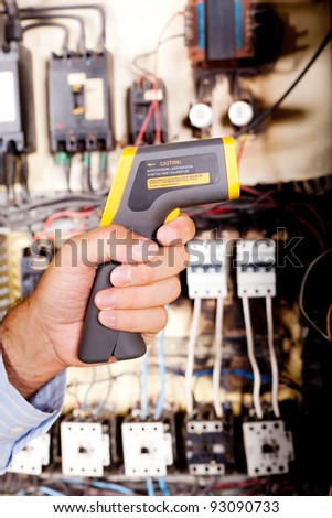 technician holding industrial laser thermometer in front of machine