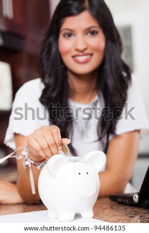 beautiful young indian woman putting a coin in piggy bank, focus on foreground