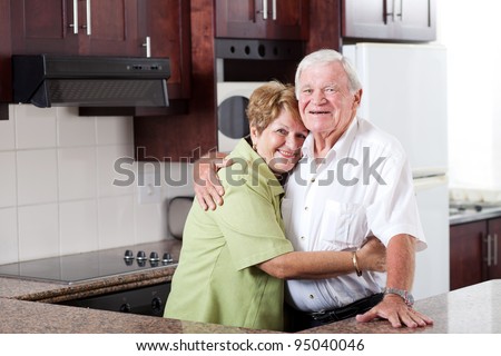 happy elderly couple hugging in home kitchen