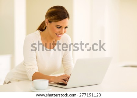 happy young woman reading emails on laptop computer in the kitchen